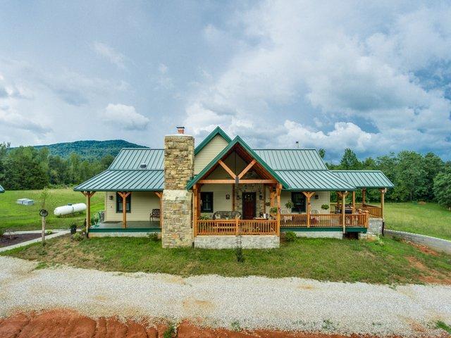 photo of log home with green metal roofing, wrap around porches, outside stone fireplace and a-frame porch