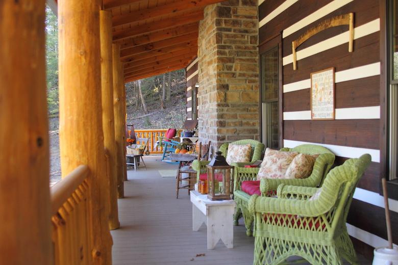 photo of wide chink log home exterior with porch with giant log support beams and round log rails