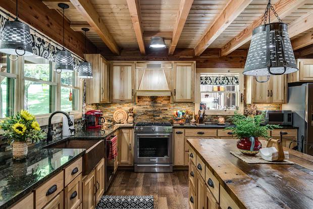 photo of log home master kitchen with exposed beam ceiling, wood flooring and wood cabinets large wood island and farm sink